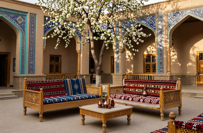 Traditional Tajik courtyard with blue tile work, carved wooden pillars, and colorful suzani textiles in warm afternoon light